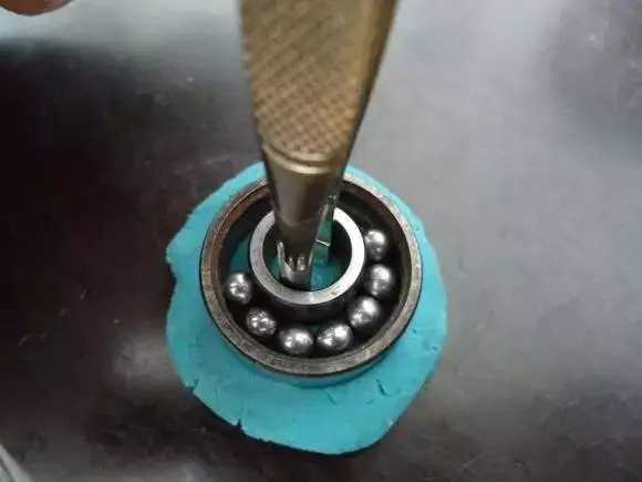 用鑷子或別的相近的物體越過內圈，同時向滾珠的方向用力頂住